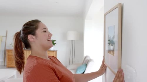 Woman Decorating Home Interior Hanging Picture on Wall