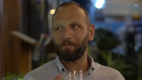 Happy caucasian man enjoys a refreshing beer alone at a late night cafe