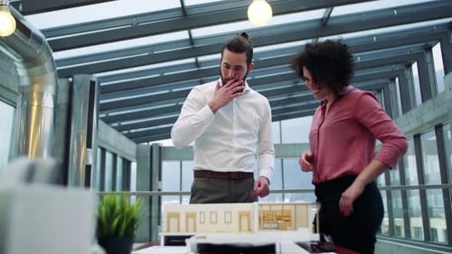 Architects With Model Of A House Standing In Office, Talking.