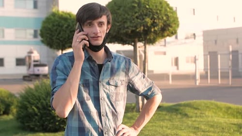 Isolated Handsome Man Sitting in Park in Medical Mask and Using Smartphone