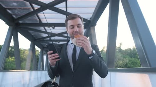 A Businessman Walking Down the Street and Eating Fast Food