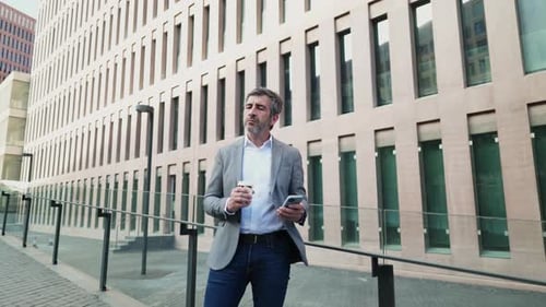 Man Holding Coffee Using Smartphone in City