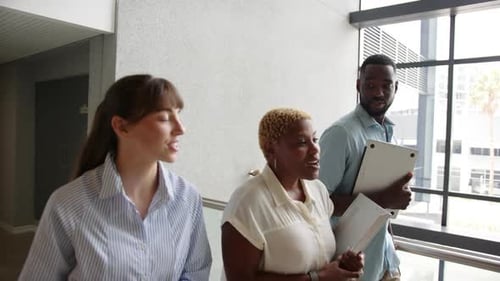 Walking in office, diverse colleagues discussing work while holding documents and laptop