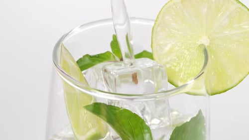 Close Up Of Fresh Lime Soda Being Poured Into A Glass With Mint, Sliced Lime And Ice