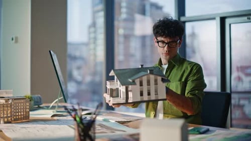 Architect Examining House Model Working on Architectural Project in Office