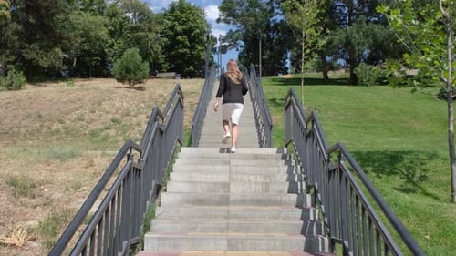 beautiful young business woman or office worker walking up the stairs in the park holding smartphone