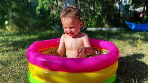 Adorable baby boy sitting in the bright inflatable pool. Water is poured on the child from top.