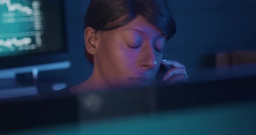 Courtière en valeurs mobilières travaillant tard dans la nuit à négocier et parlant au téléphone derrière un ordinateur
