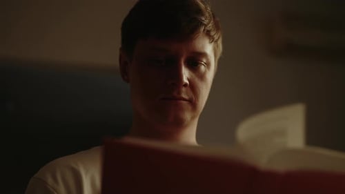 Closeup Lowangle View of Young Man Reading Paper Book Turning Pages Sitting in Dark Living Room