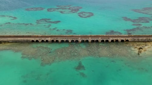 Aerial view of car bridge over turquoise water on tropical island. PULLBACK.