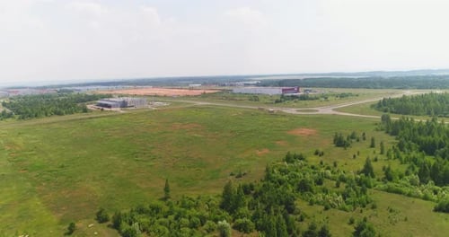 Large Green Field and Storehouse Buildings Under Cloudy Sky