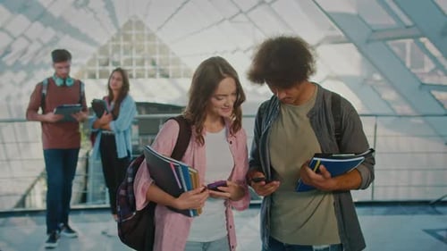 Two Students Talking and Using Smartphone in the College Hallway