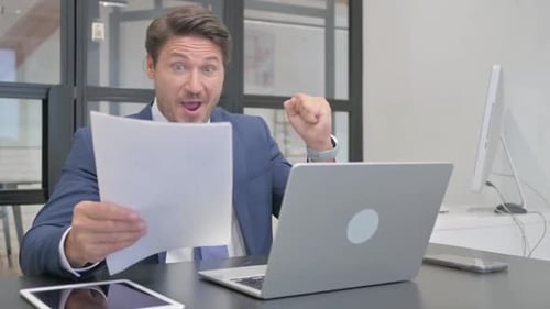 Man Celebrates Reading Document at Desk in Office