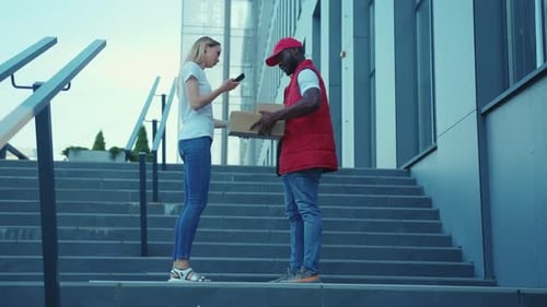 On Stairs African American Delivery Man Hold Package Woman Client Paying By Phone for Parcel
