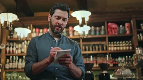 Man Writing in Notepad Behind Cafe Counter