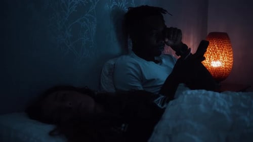 Un homme se frotte les yeux de fatigue alors qu'il est assis dans son lit la nuit à l'aide d'un téléphone intelligent