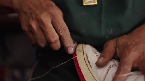 Nahaufnahme der Hände eines erfahrenen Schuhmachers, der die Sohle eines Sportschuhs mit einer Ahle näht und