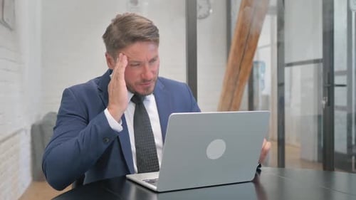 Man Rubbing His Head While Working on Laptop