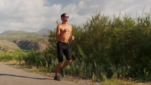 Young Runner Jogs Through Mountain Slopes Sunlight Highlighting His Body