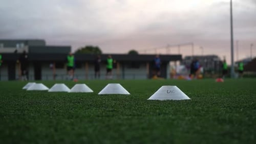 A yellow disc rolls past a group of young people on a grass field football training