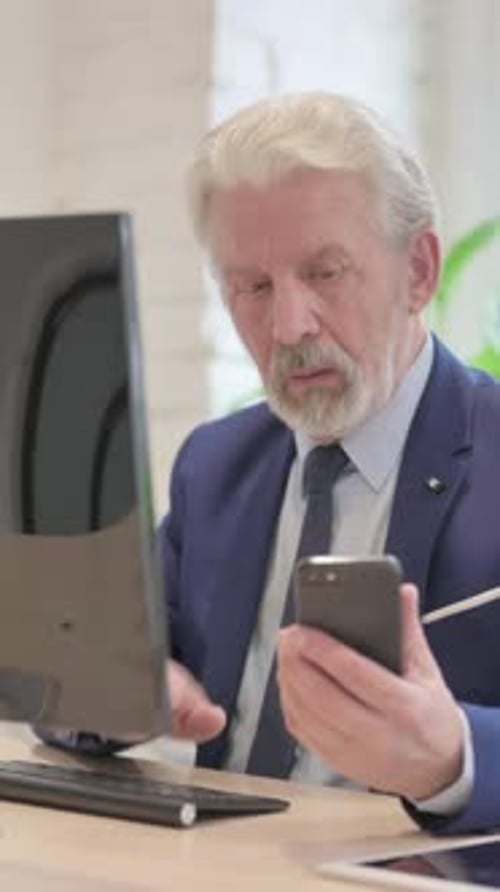 Senior Man Typing at Computer and Using Phone