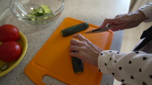 Person Cuts Cucumber on Orange Cutting Board