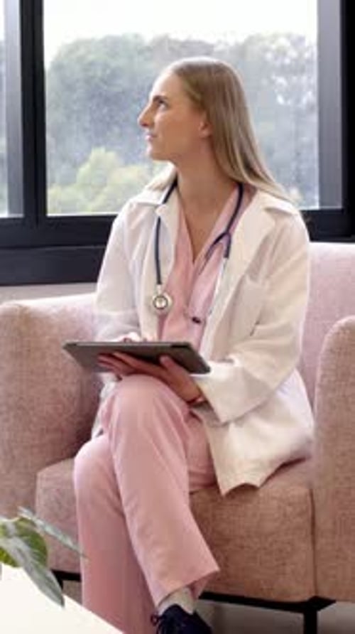 Vertikales Video: Ich sehe Hügel in der Klinik, Krankenschwester in rosafarbenem Peeling, passt das Tablet an und tippt auf Notizen