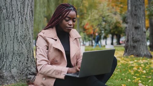 Smiling Woman Working on Laptop in Autumn Park
