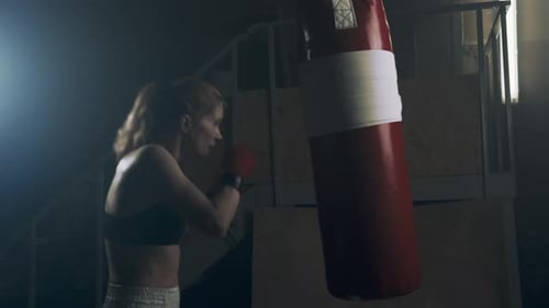 Woman Boxing with Punching Bag in Dark Gym