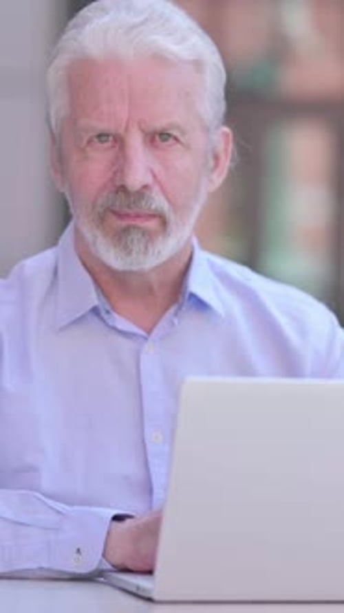 Senior Man Uses Laptop At Table Indoors