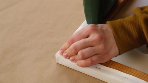 Hands Securing Canvas to Wood Frame with Staple Gun