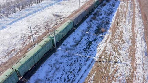 Flight over the roofs of freight cars of a moving train with snow on the side