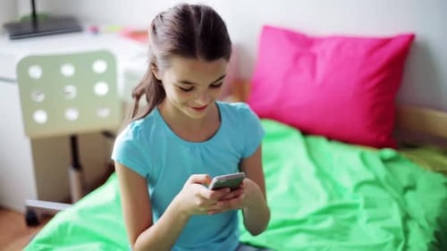 Smiling girl on bed with smartphone in bedroom
