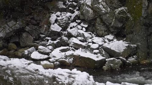 Dramatic Scene Of A Falling Snow On Rocky River. Slow Motion