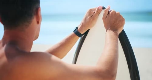 Brazilian male surfer stands with surf board on the beach