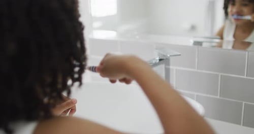 Un garçon biracial se brosse les dents dans une salle de bain lumineuse