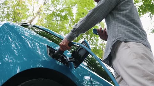 Young man charging electric car outdoor at green forest. Save ecology alternative energy sustainable