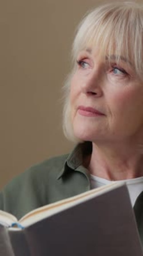 Calm Peaceful Caucasian Old Woman Reading Book Enjoying Read Literature at Home Looking Away