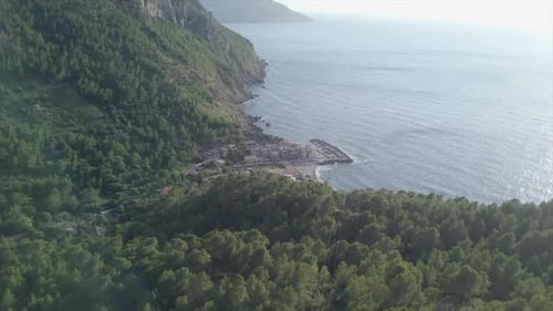 A Drone Approaches Slowly From Above to a Small Seacoast Village Surrounded By Trees
