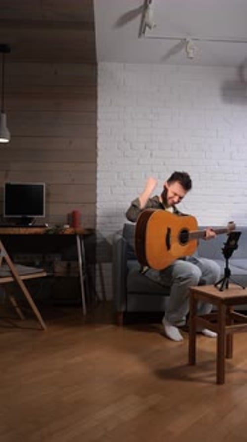 Vertical Video Frustrated Man Sitting on a Sofa with His Acoustic Guitar Having an Online Music