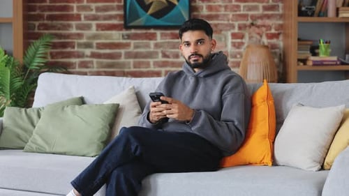 Man Using Phone Relaxing on Gray Couch Indoors