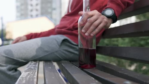 A man with alcohol addiction in a depressed state holds a bottle of wine in his hands.
