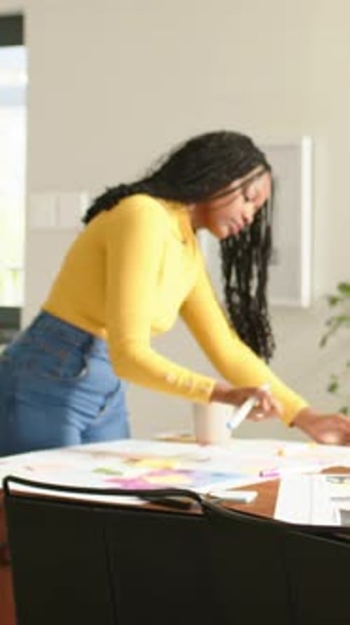 Vidéo verticale : Inspection d'une planche à papier, femme en jaune déplaçant des notes autocollantes, marquant un plan à la maison