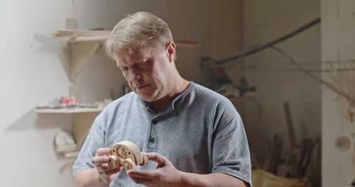 Carpenter in His Own Home Workshop Inspects a Handmade Wooden Toy for His Grandch and Thinks to