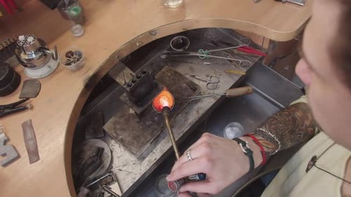Ein Mann arbeitet an einem Schmuckstück mit einer Fackel, um einen Metallgegenstand zu erhitzen