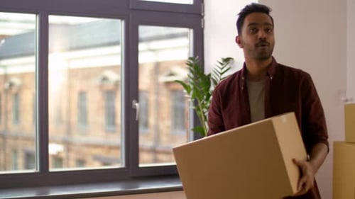 Man Carrying Cardboard Box Into New Home Indoors