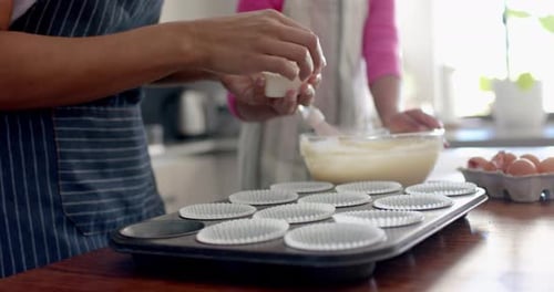 Mittelteil einer birazialen Mutter und Tochter, die in der Küche Cupcakes backen, Kopierraum, Zeitlupe