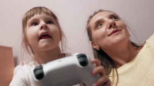 Little Girl is Playing Video Games on a Console with Her Mom Holding a Modern Controller