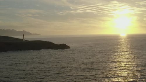 Drohnenaufnahme eines Leuchtturms zur goldenen Stunde mit Meer und Sonne im Hintergrund