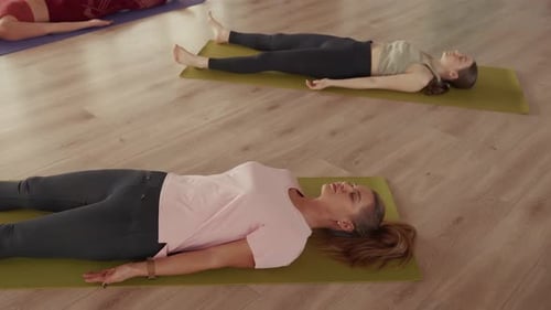 Women Relaxing in Savasana Pose During Yoga Class in Studio